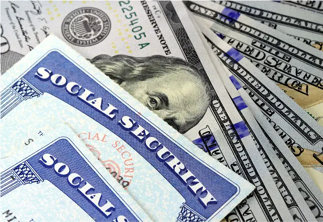 Close-up of Social Security cards placed on top of U.S. dollar bills, including a $20 bill featuring Abraham Lincoln's portrait.